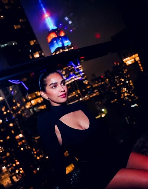 A woman posing against a window overlooking the illuminated Manhattan skyline at Suave Saturdays.