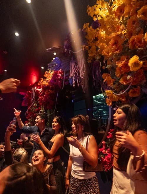Group of women raising drinks and enjoying the night, surrounded by vibrant floral decorations at Suave Saturdays.
