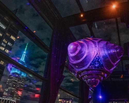 View of the Empire State Building lit up at night, with a large disco ball and partygoers in the rooftop venue of Suave Saturdays.