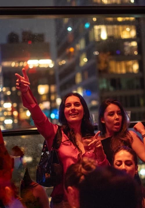 Woman in a red blouse raising her hand and smiling, enjoying the lively rooftop atmosphere at Suave Saturdays.